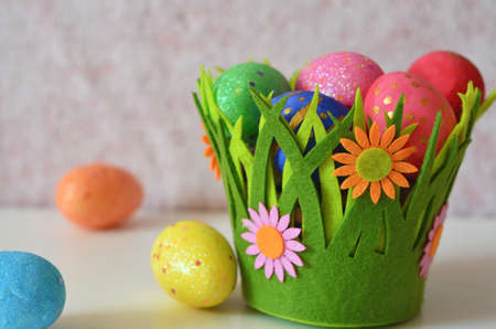 Happy Easter Day. Easter eggs concept. Closeup Colorful Easter eggs in nest and basket green gress on white wooden backgroundの写真素材
