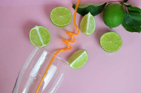 Ingredients for making mojito on a pink background. Empty glass, straw, mint, lime, ice cubes. lime and mint falling into a cocktail splashingの写真素材