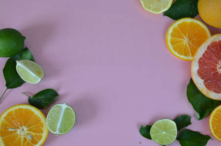 Flat lay of citrus fruits like lime and lemon with lemon tree leaves on light pink background making a frameの写真素材