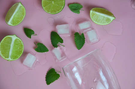 Ingredients for making mojito on a pink background. Empty glass, straw, mint, lime, ice cubes. lime and mint falling into a cocktail splashingの写真素材