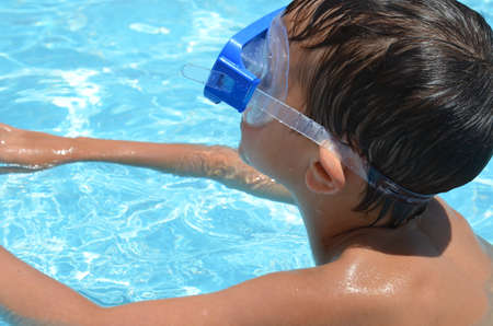 Teenager boy wearing mask swimming in the pool. Happy holiday concept. Cute happy little boy swimming and snorking in the sea ocean in crystal blue waterの写真素材