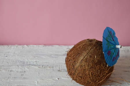 whole coconut on white wooden background, pink background with blue umbrella for a cocktail. concept...