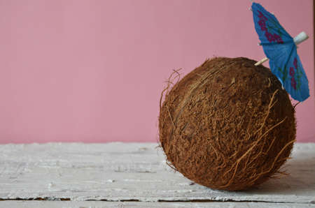 whole coconut on white wooden background, pink background with blue umbrella for a cocktail. concept...