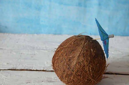 whole coconut on white wooden background, pink background with blue umbrella for a cocktail. concept...