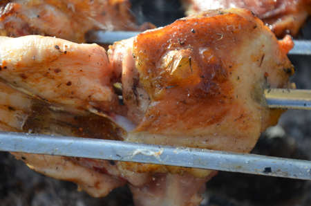closeup of some meat skewers being grilled in a barbecue. pieces of chicken leg meat roasting on the corners of skewers.の写真素材
