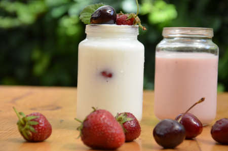 Healthy breakfast - granola, strawberries, cherry, honeysuckle berry, nuts and yogurt in a bowl. Vegetarian concept food. Top view pudding or cocktail on the background of green foliage.の写真素材