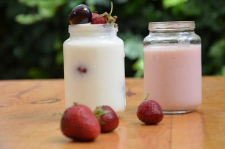 Healthy breakfast - granola, strawberries, cherry, honeysuckle berry, nuts and yogurt in a bowl. Vegetarian concept food. Top view pudding or cocktail on the background of green foliage.の写真素材