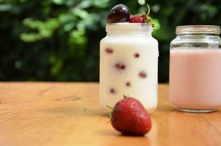 Healthy breakfast - granola, strawberries, cherry, honeysuckle berry, nuts and yogurt in a bowl. Vegetarian concept food. Top view pudding or cocktail on the background of green foliage.の写真素材