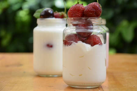 Healthy breakfast - granola, strawberries, cherry, honeysuckle berry, nuts and yogurt in a bowl. Vegetarian concept food. Top view pudding or cocktail on the background of green foliage.の写真素材
