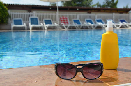 Sunscreen in a yellow jar with sunglasses on a background of blue pool water. The concept of rest, enjoying the sun, tanning, relaxationの写真素材