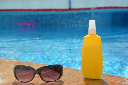 Sunscreen in a yellow jar with sunglasses on a background of blue pool water. The concept of rest, enjoying the sun, tanning, relaxationの写真素材
