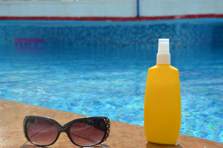 Sunscreen in a yellow jar with sunglasses on a background of blue pool water. The concept of rest, enjoying the sun, tanning, relaxationの写真素材