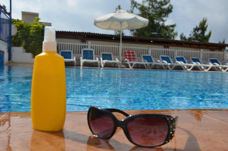 Sunscreen in a yellow jar with sunglasses on a background of blue pool water. The concept of rest, enjoying the sun, tanning, relaxationの写真素材