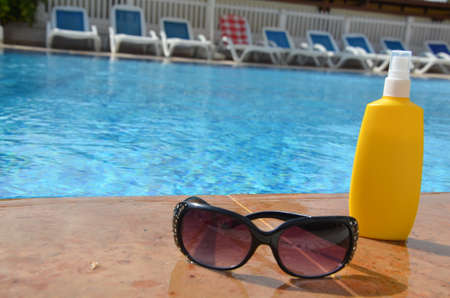 Sunscreen in a yellow jar with sunglasses on a background of blue pool water. The concept of rest, enjoying the sun, tanning, relaxationの写真素材