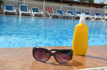 Sunscreen in a yellow jar with sunglasses on a background of blue pool water. The concept of rest, enjoying the sun, tanning, relaxationの写真素材