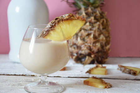 Traditional caribbean cocktail pina colada in a glasses on a blue background. Cocktail or juice with pineapple and coconut on the background in a beautiful glass on a pink, white wooden background with an umbrella.の写真素材