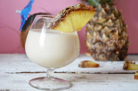 Traditional caribbean cocktail pina colada in a glasses on a blue background. Cocktail or juice with pineapple and coconut on the background in a beautiful glass on a pink, white wooden background with an umbrella.の写真素材