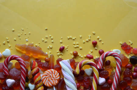 candies with jelly and sugar. colorful array of different childs sweets and treats on yellow background. red marmalade in the shape of a heart with a variety of caramels and candies, marshmallows. Abstract. top view copy spaceの写真素材