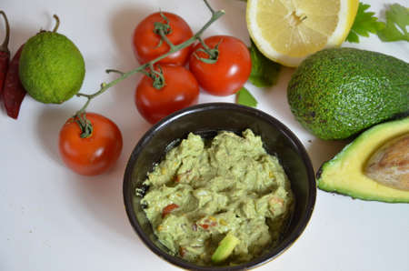 A delicious Bowl of Guacamole next to fresh ingredients on a table with tortilla chips and salsa. sandwich with guacamole, red hot pepper, lime, lemon, avocado.の写真素材