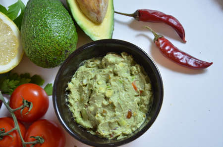 A delicious Bowl of Guacamole next to fresh ingredients on a table with tortilla chips and salsa. sandwich with guacamole, red hot pepper, lime, lemon, avocado.の写真素材