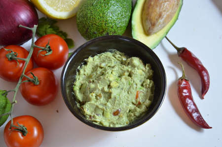 A delicious Bowl of Guacamole next to fresh ingredients on a table with tortilla chips and salsa. sandwich with guacamole, red hot pepper, lime, lemon, avocado.の写真素材