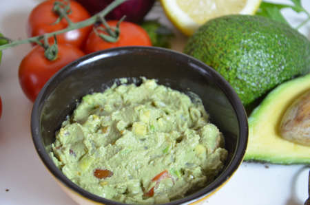 A delicious Bowl of Guacamole next to fresh ingredients on a table with tortilla chips and salsa. sandwich with guacamole, red hot pepper, lime, lemon, avocado.の写真素材