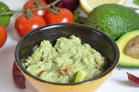 A delicious Bowl of Guacamole next to fresh ingredients on a table with tortilla chips and salsa. sandwich with guacamole, red hot pepper, lime, lemon, avocado.の写真素材