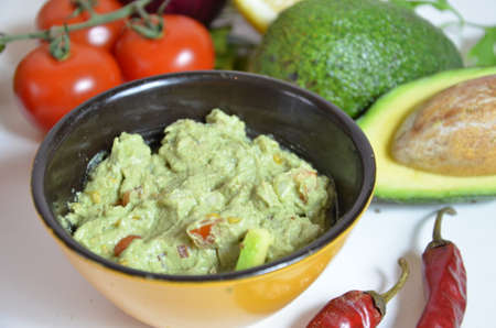 A delicious Bowl of Guacamole next to fresh ingredients on a table with tortilla chips and salsa. sandwich with guacamole, red hot pepper, lime, lemon, avocado.の写真素材