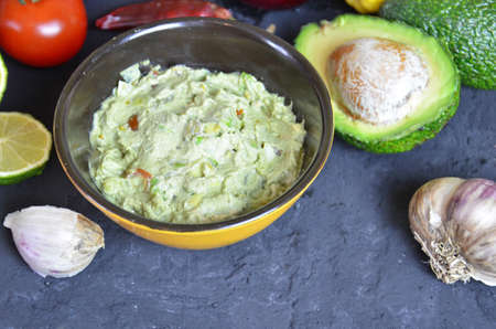Bowl of freshly prepared guacamole. Ingredients on the background tomatoes, hot pepper, lime, avocado Guacamole nachos and guacamole ingredients on dark wooden background.の写真素材