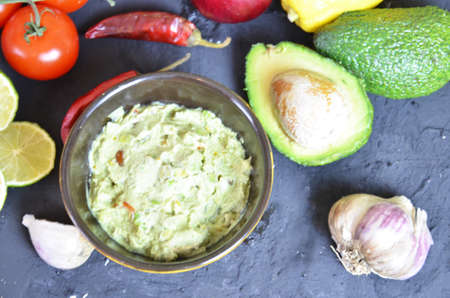 Bowl of freshly prepared guacamole. Ingredients on the background tomatoes, hot pepper, lime, avocado Guacamole nachos and guacamole ingredients on dark wooden background.の写真素材
