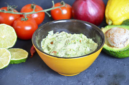 Bowl of freshly prepared guacamole. Ingredients on the background tomatoes, hot pepper, lime, avocado Guacamole nachos and guacamole ingredients on dark wooden background.の写真素材
