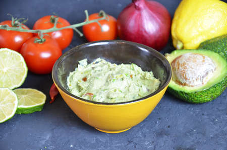 Bowl of freshly prepared guacamole. Ingredients on the background tomatoes, hot pepper, lime, avocado Guacamole nachos and guacamole ingredients on dark wooden background.の写真素材