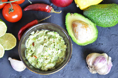 Bowl of freshly prepared guacamole. Ingredients on the background tomatoes, hot pepper, lime, avocado Guacamole nachos and guacamole ingredients on dark wooden background.の写真素材
