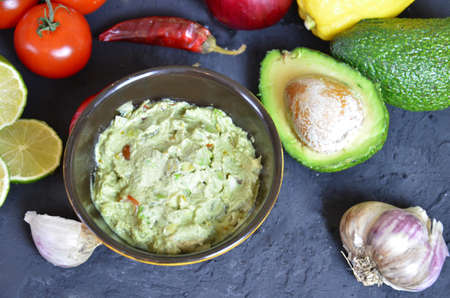 Bowl of freshly prepared guacamole. Ingredients on the background tomatoes, hot pepper, lime, avocado Guacamole nachos and guacamole ingredients on dark wooden background.の写真素材