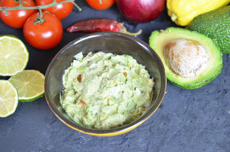 Bowl of freshly prepared guacamole. Ingredients on the background tomatoes, hot pepper, lime, avocado Guacamole nachos and guacamole ingredients on dark wooden background.の写真素材