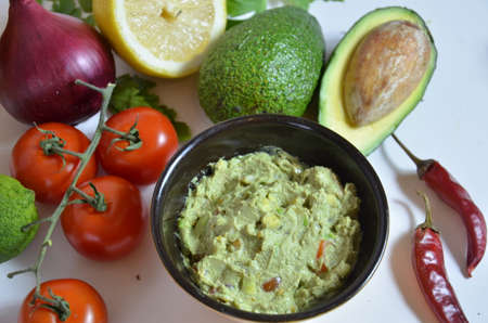 A delicious Bowl of Guacamole next to fresh ingredients on a table with tortilla chips and salsa. sandwich with guacamole, red hot pepper, lime, lemon, avocado.の写真素材