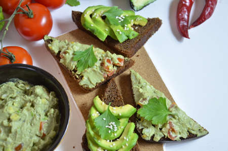 A delicious Bowl of Guacamole next to fresh ingredients on a table with tortilla chips and salsa. sandwich with guacamole, red hot pepper, lime, lemon, avocado.の写真素材