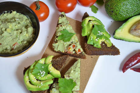 A delicious Bowl of Guacamole next to fresh ingredients on a table with tortilla chips and salsa. sandwich with guacamole, red hot pepper, lime, lemon, avocado.の写真素材