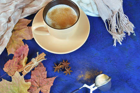 Autumn cappuccino composition. coffee cup top view with foam, cloves, cinnamon, autumn fallen leaves and scarf . Fall hot drinks conceptの写真素材