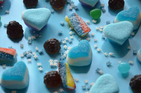An assortment of colourful, festive sweets, blue marmalade in the shape of a heart on a blue background with a variety of caramels and candies, marshmallows. Abstract background. top view copy space.の写真素材