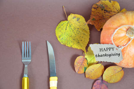Thanksgiving Day. Pumpkin, pumpkin with autumn leaves and apples. Autumn harvest on a brown background. Happy Thanksgiving Lettering set table for celebration. fork and knife.の写真素材