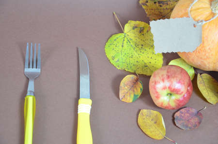 Thanksgiving Day. Pumpkin, pumpkin with autumn leaves and apples. Autumn harvest on a brown background. Happy Thanksgiving Lettering set table for celebration. fork and knife.の写真素材