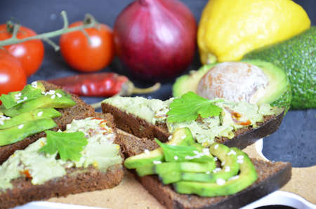 Guacamole with bread and avocado Sandwich with avocado and guacamole. Black cereal bread. Ingredients for making lime, red pepper, tomatoes. Healthy food, diet on a black background.の写真素材