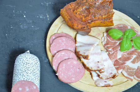 Assortment of salami and snacks. Sausage Fouet, sausages, salami, paperoni. On a black and wooden background. Top view. Free space for your textの写真素材