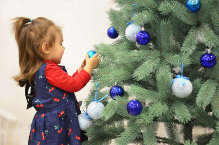 Back view of toddler girl decorating Christmas tree, tree with blue balls on a white backgroundの写真素材