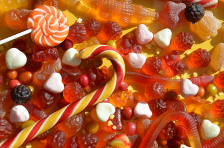 candies with jelly and sugar. colorful array of different childs sweets and treats on yellow background. red marmalade in the shape of a heart with a variety of caramels and candies, marshmallows. Abstract. top view copy spaceの写真素材