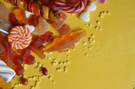 candies with jelly and sugar. colorful array of different childs sweets and treats on yellow background. red marmalade in the shape of a heart with a variety of caramels and candies, marshmallows. Abstract. top view copy spaceの写真素材