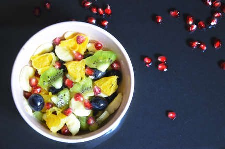 salad with fresh fruits and berries made from orange grapes and pomegranate and kiwi on a black background diet healthy nutrition vegetarianism.の写真素材