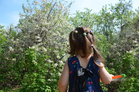 beautiful girl stands among the flowering trees. Lovely cute little girl in red sunglasses spring blooming garden a tree with white flowers. Happy childhood, the awakening of nature Portrait Romanceの写真素材
