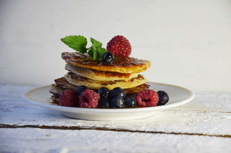 Pancakes with berries and maple syrup in a plate on a white wooden background.の写真素材